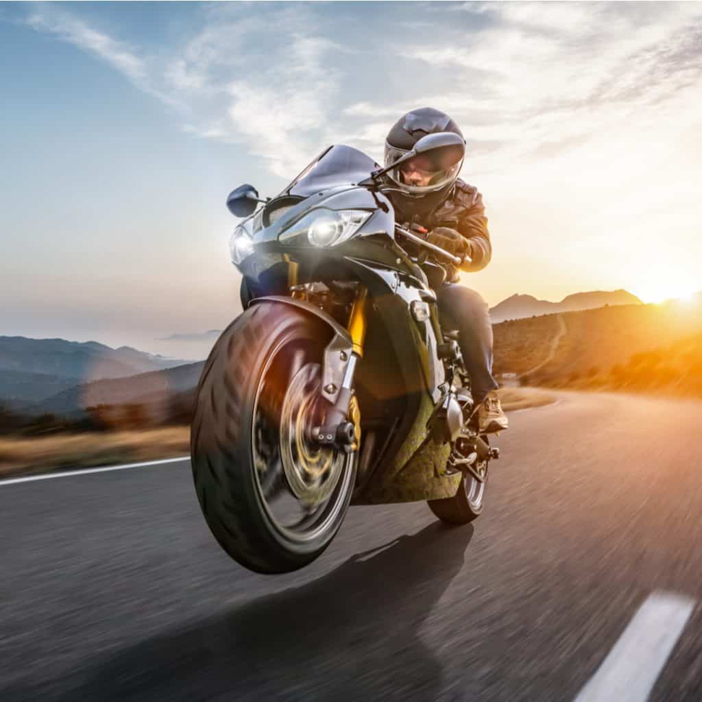 A motorcycle carries its rider down a twisty road on sunset.