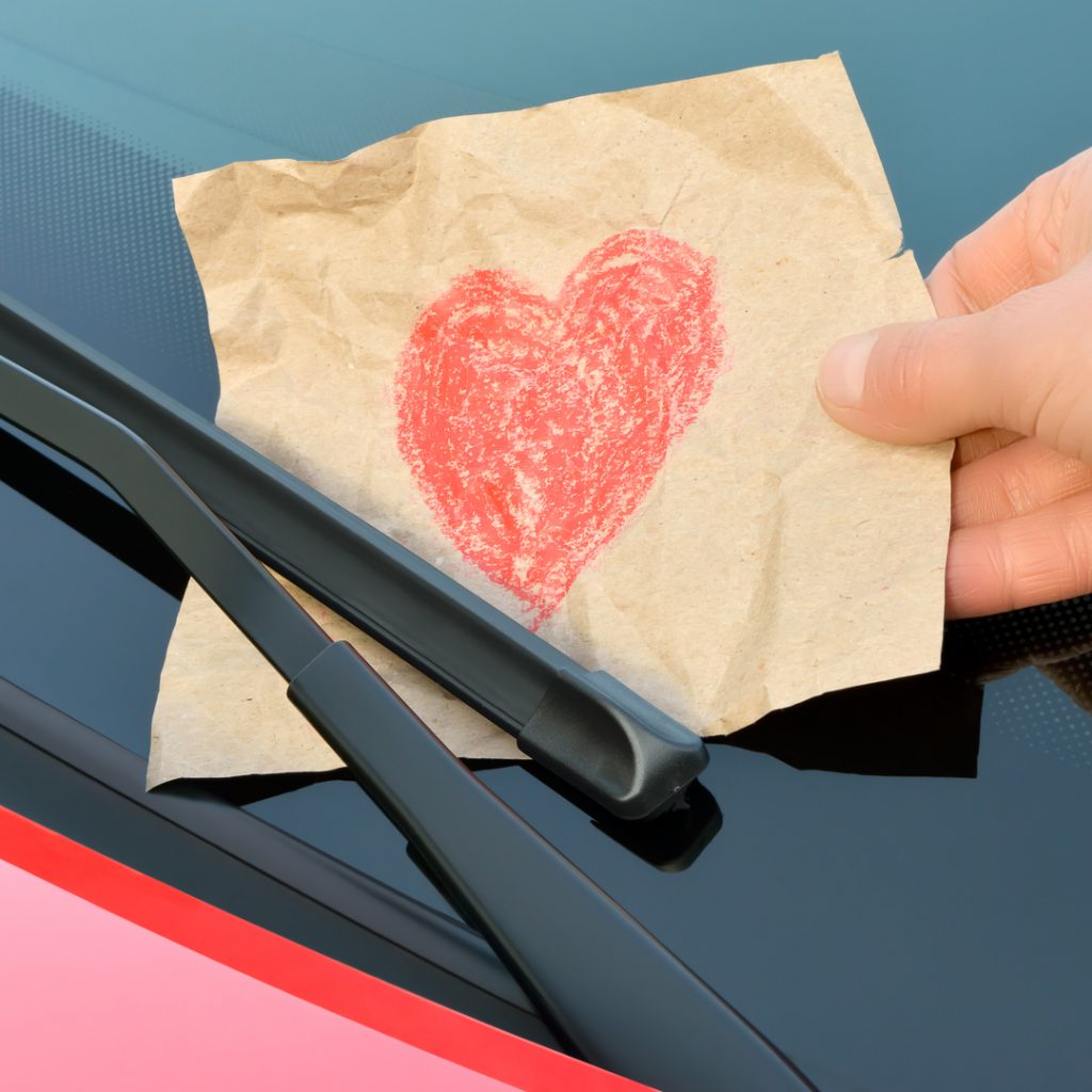 Someone puts a handmade Valentine's Day card under the wipers of valentine's car.