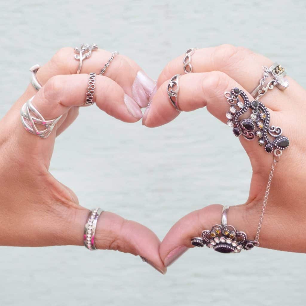 Two hands adorned with rings and fine jewelry make a heart shape.