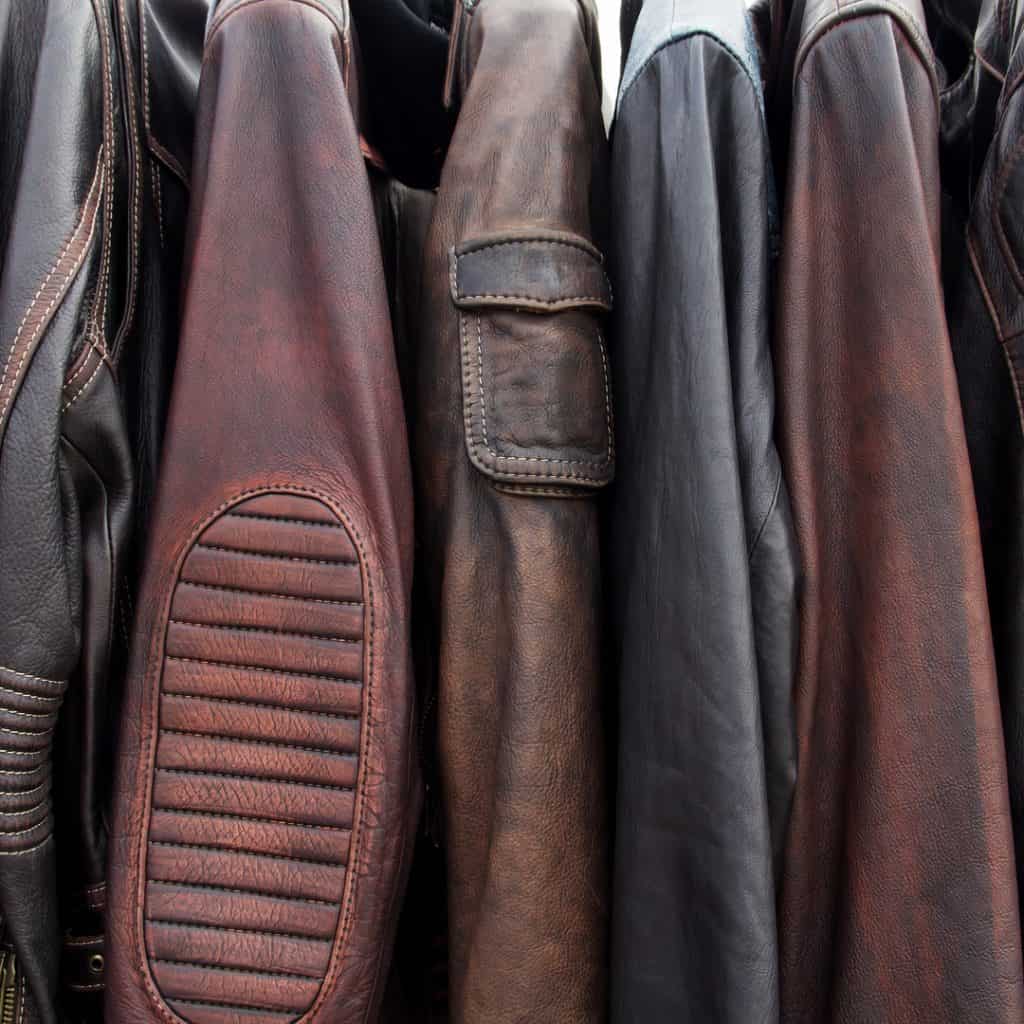 A row of worn brown and black leather jackets hang in a row.