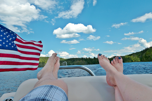 Two people relax on a pontoon boat on a lake in America.