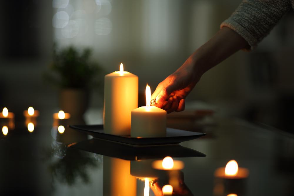A hand lights a large candle situated on a table.