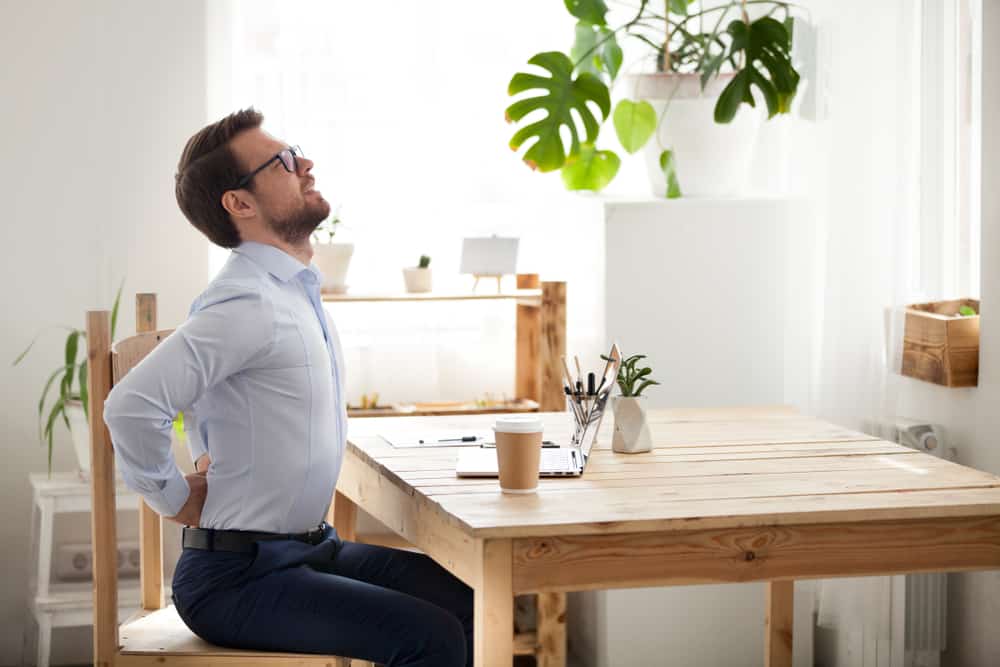 A man grabs and stretches his sore lower-back while at work.