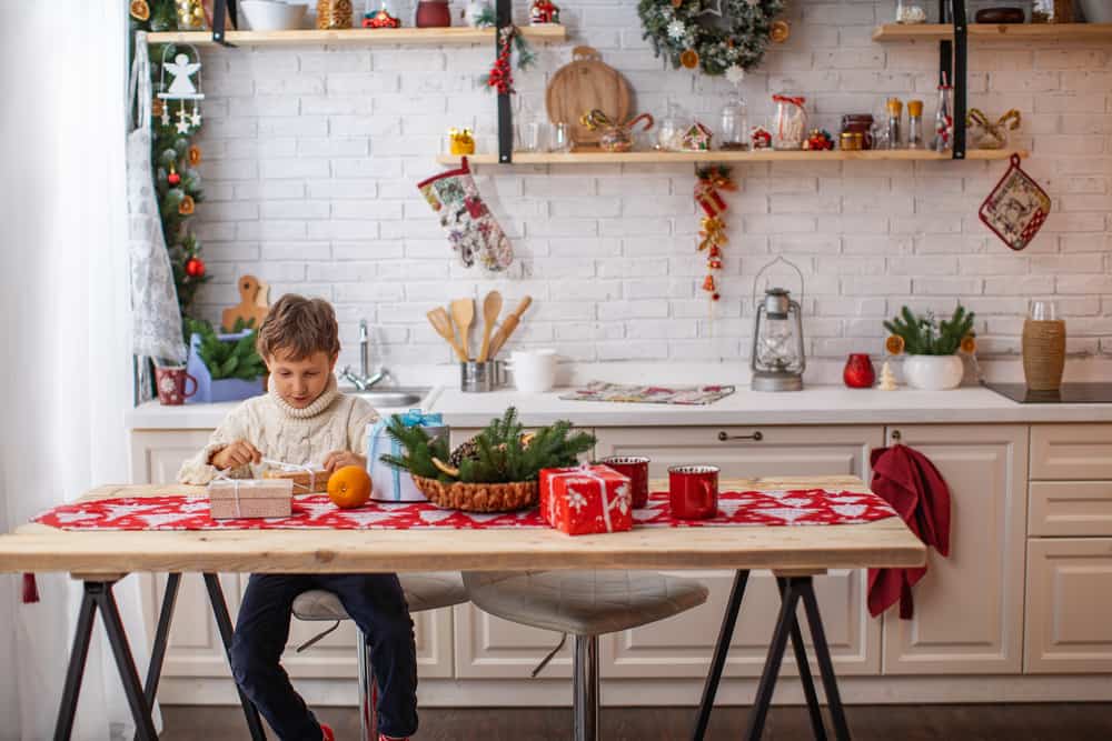 A boy sits at a dining table and wraps Christmas presents.