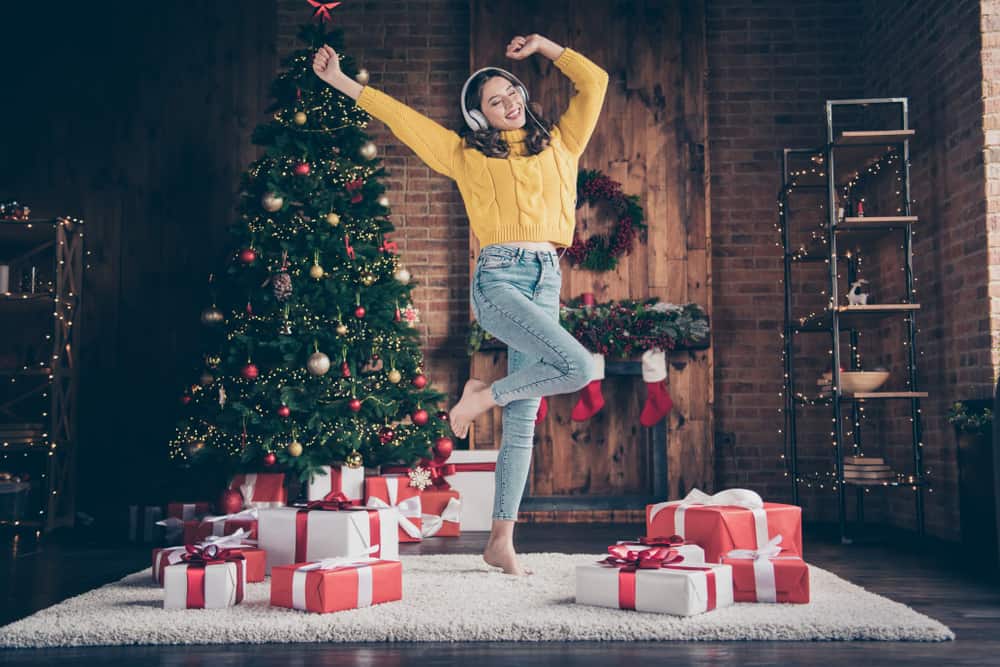 A woman dances with headphones under a Christmas tree.