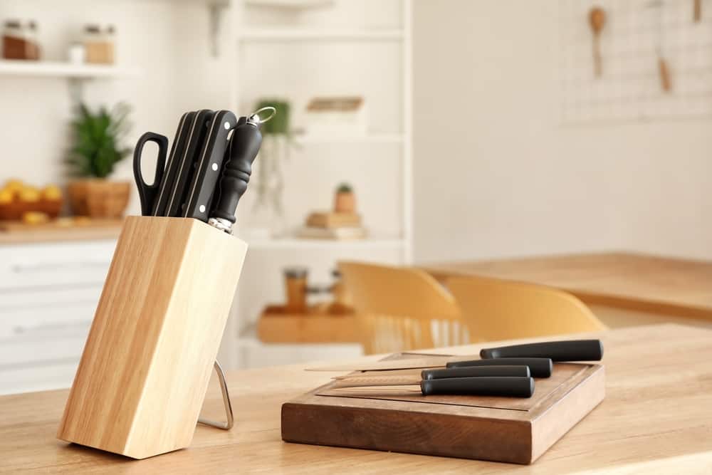 A nice knife set sits in a kitchen on top of a cutting block.